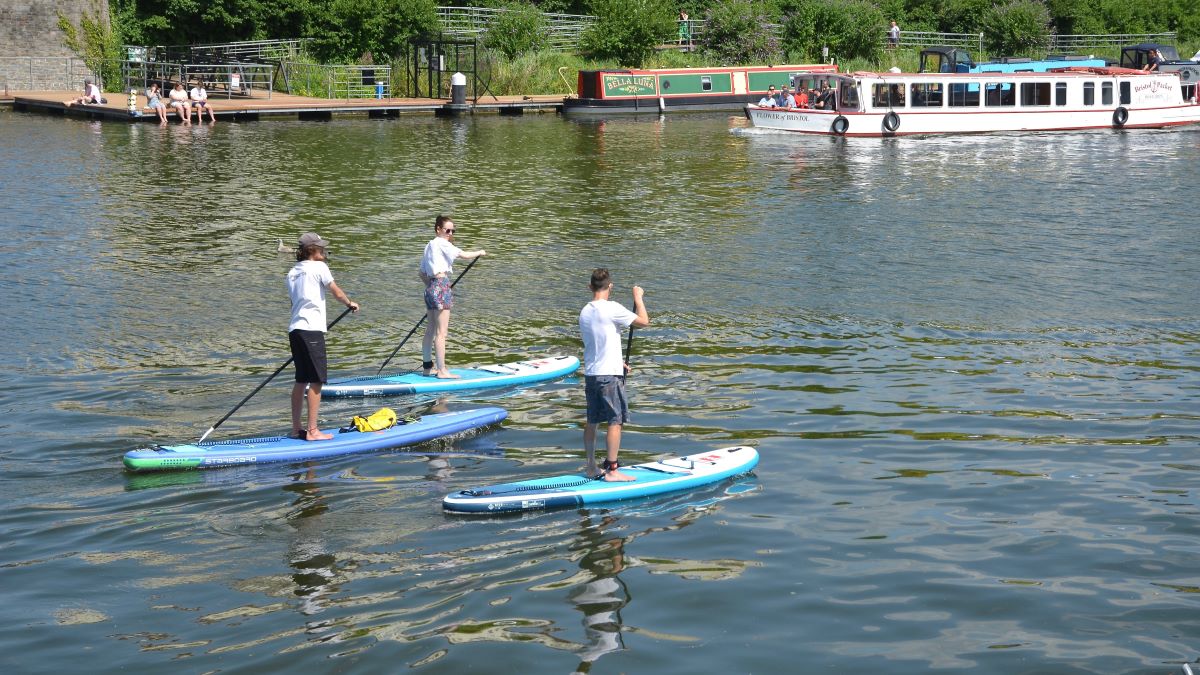 Three people travelling down Bristol Harbour on paddleboards