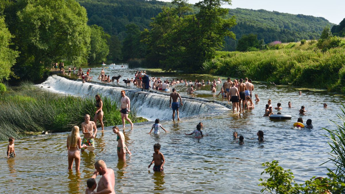 People walking across and swimming and enjoying the good weather in River Avon on a busy day. Warleigh Weir, offering outdoor swimming near Bristol