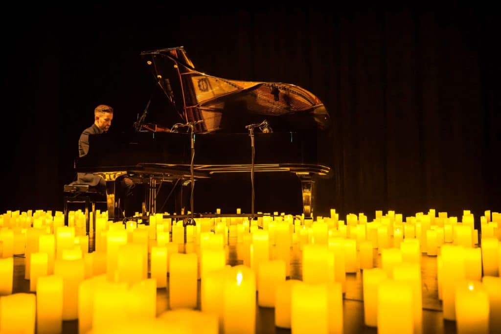 A man playing the piano surrounded by hundreds of candles.