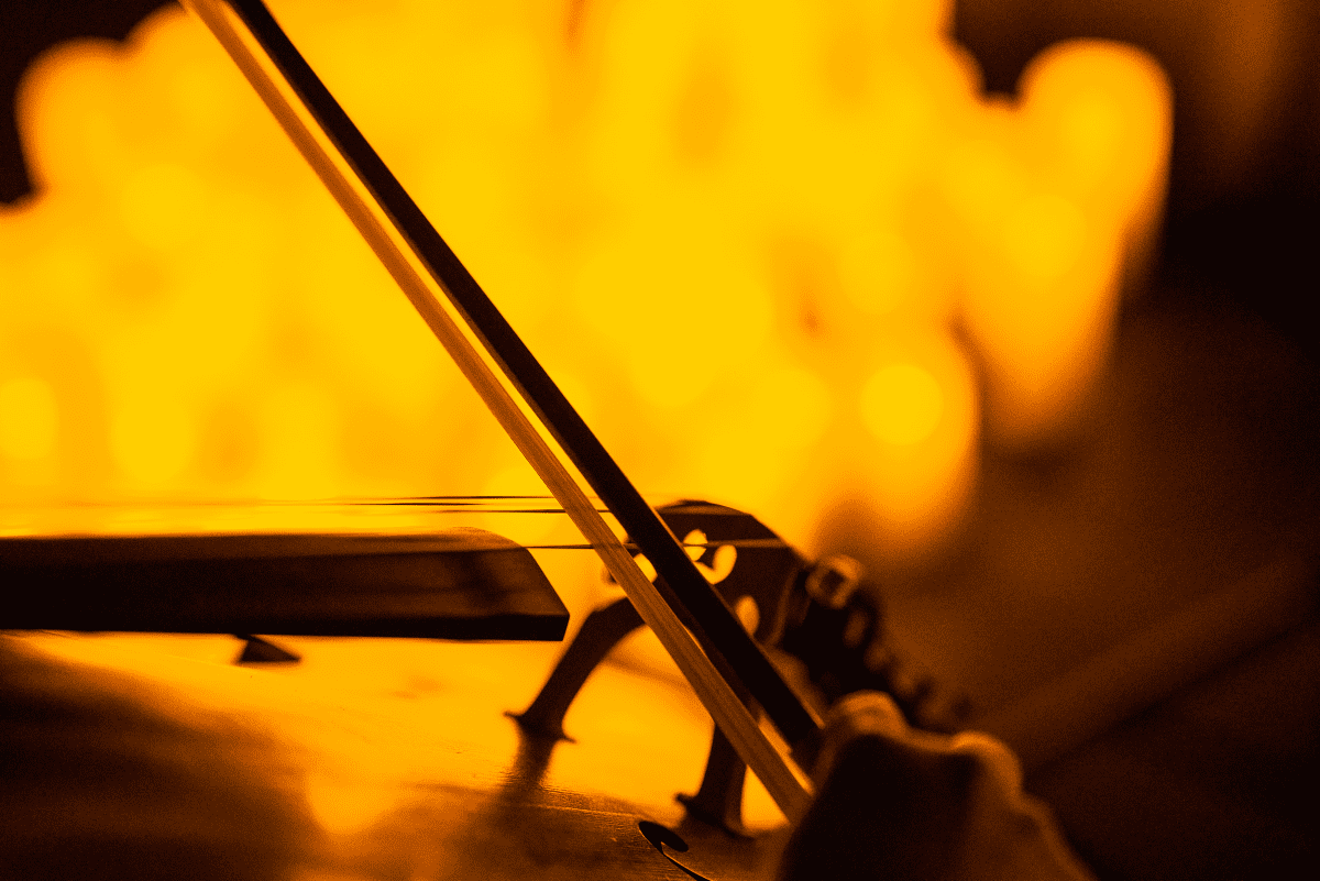 Close-up of a cello's strings and bow with the blurry glow of candles in the background.