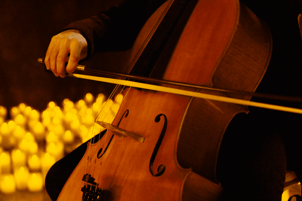 A close-up of a cello being played with candles in the background.