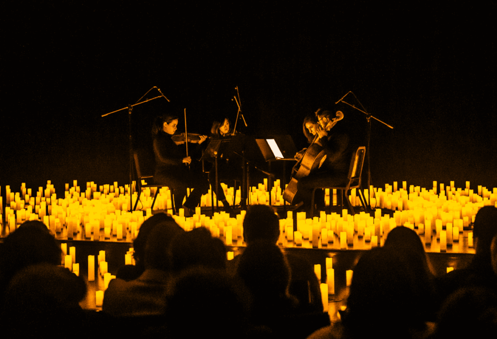 A string quartet performing on stage surrounded by candles and the silhouette of the audience visible in the foreground.
