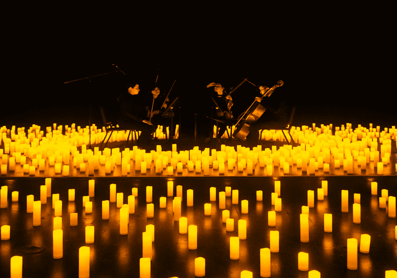 A string quartet performing at the center of a stage surrounded by candles.