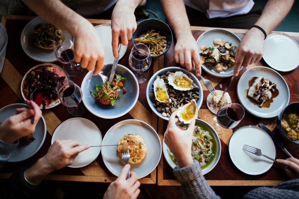 Hands reaching over table at Root for different plated of veg-based dishes