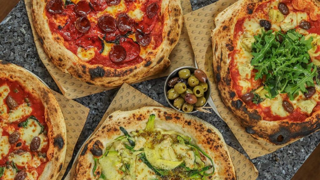 Four Pizzarova pizza sat on a table with a pot of olives