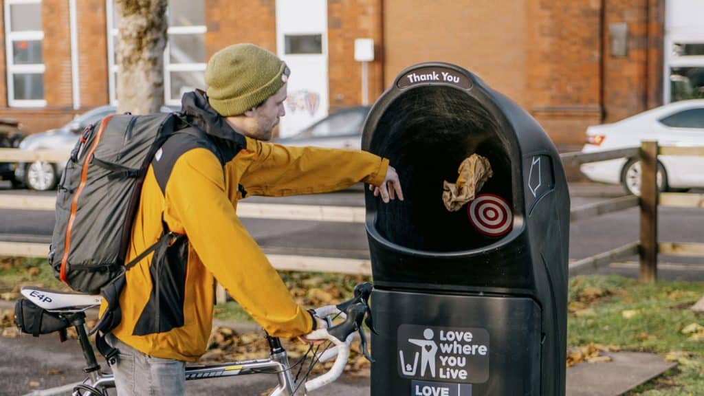 A person on a bike throwing rubbish in a bin for Bristol's Binning