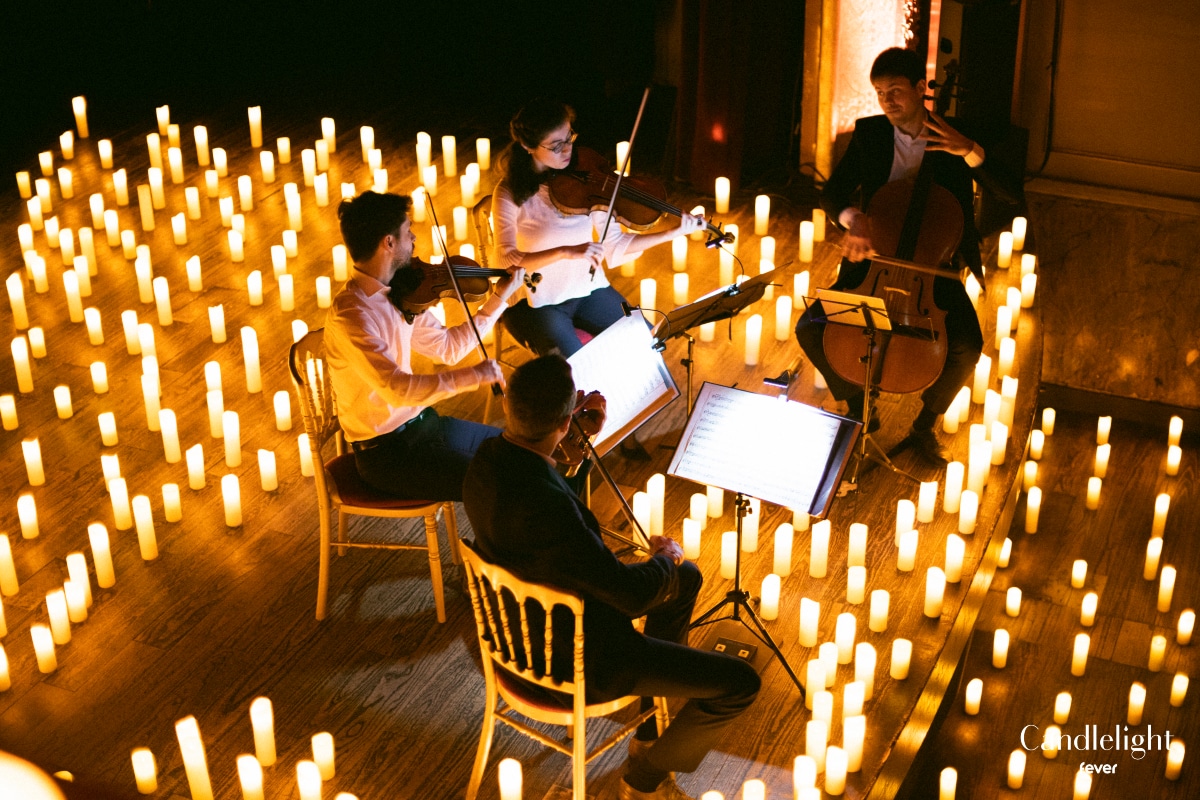 Three violinists and one cellist playing music in concert surrounded by candles