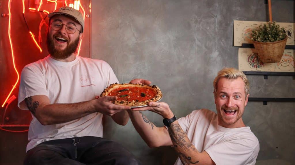 Two people from Pizzarova holding up a vegan pizza from their Veganuary menu
