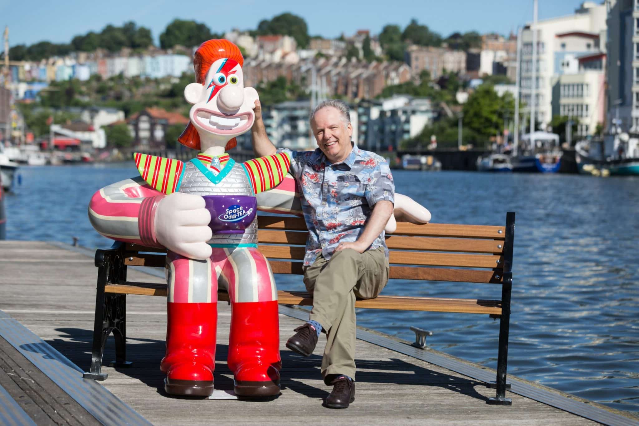 A man sat with a giant Wallace sculpture at Gromit Unleashed, Bristol. 