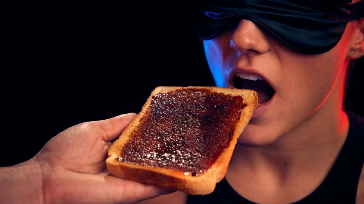 A blindfolded woman eating Marmite toast in a dark room