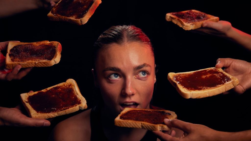 A woman surrounded by Marmite toast in a dark room