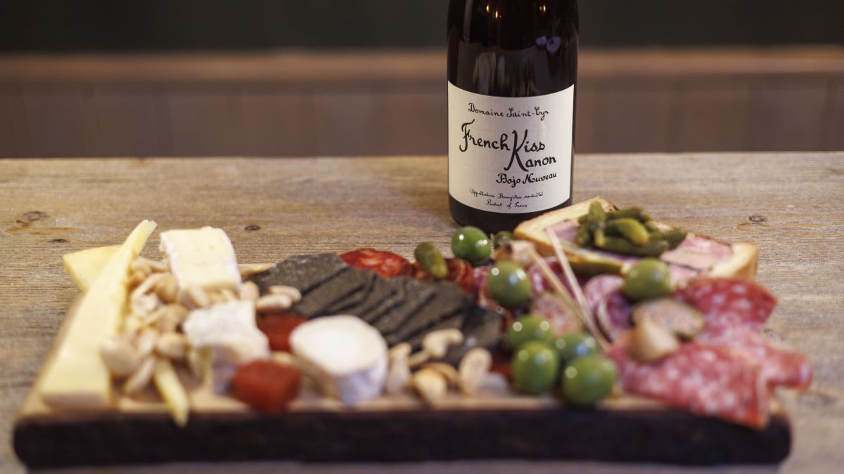 A bottle of Beaujolais nouveau with a spread of meat, cheese and grapes